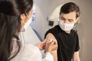 Nurse applying band-aid to patient's arm after giving a vaccination. Both nurse and patient are wearing surgical masks.