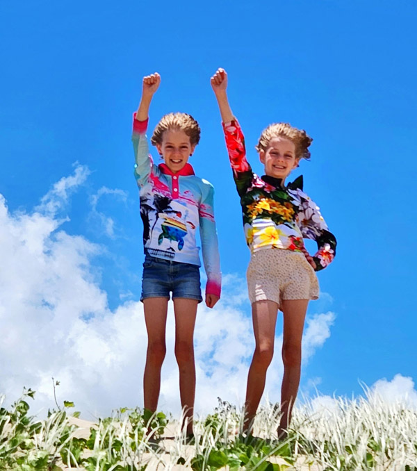 Twin sisters standing on sand hill with right hands raised triumphantly in the air