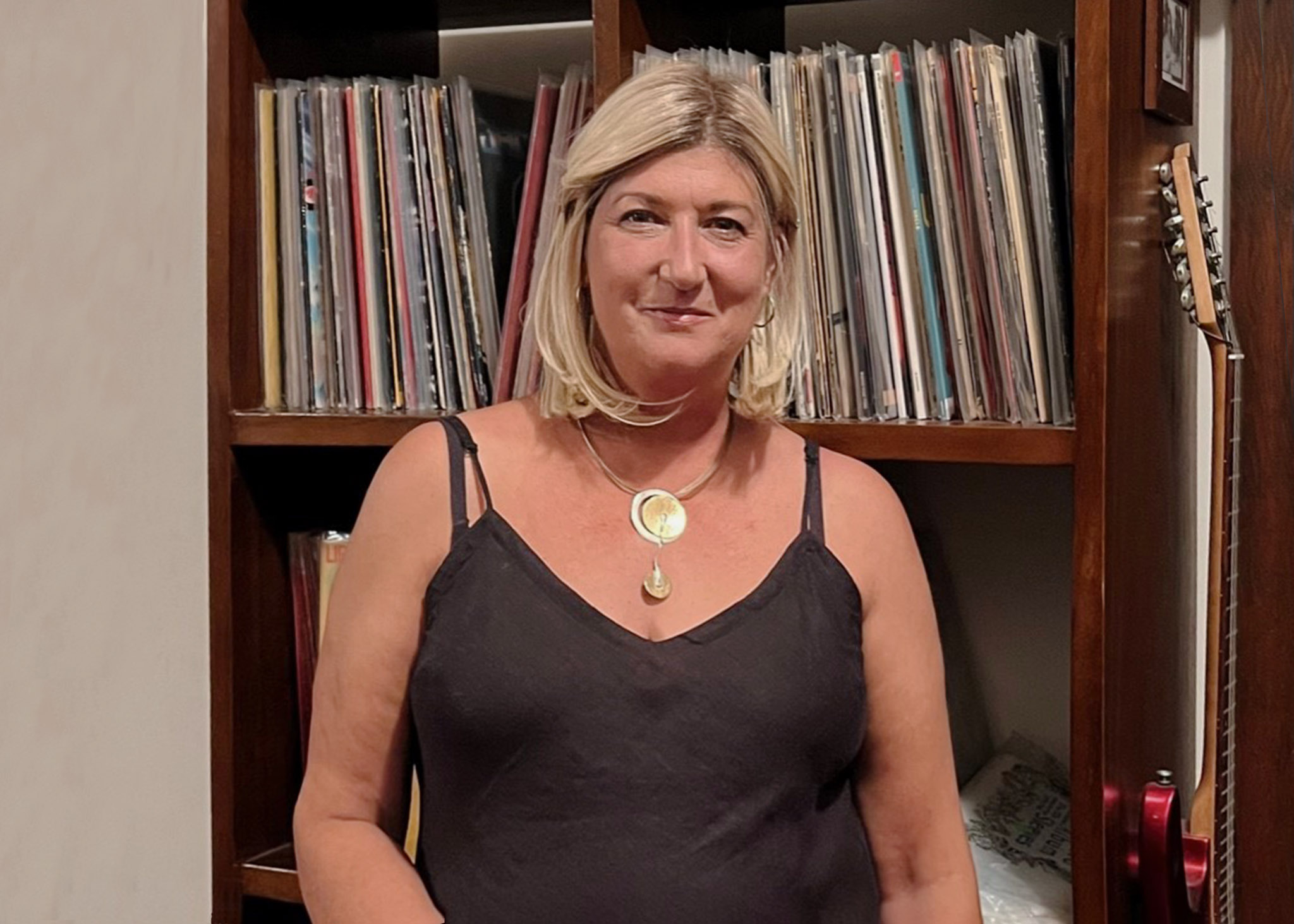 Blondes have more fun! Woman wearing blonde shoulder-length wig, standing in front of a bookshelf.