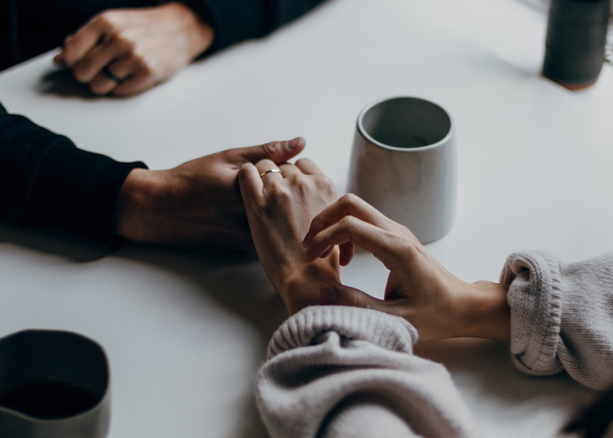 Hardship can happen to anyone. Arrow really matters: we support people during and after bone marrow transplant. Picture shows holding hands across the table. Coffee cup nearby